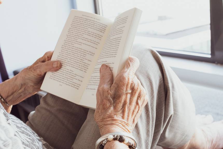 Ältere Person liest ein Buch, ihre Hände sind zu sehen.