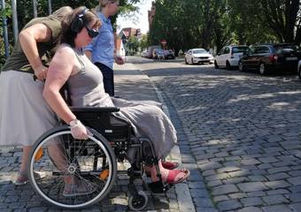 Eine Teilnehmerin möchte im Rollstuhl die Straße überqueren, der Bordstein ist nicht abgesenkt. © Johanna Michelis