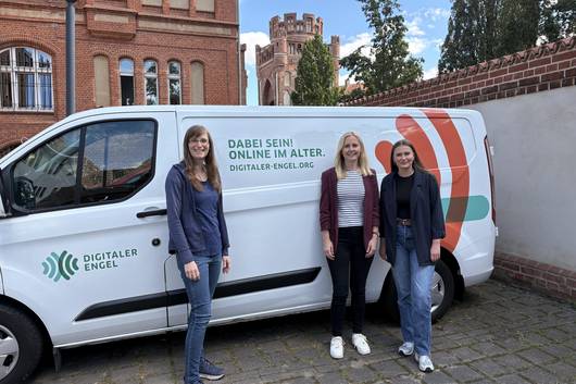 Digitalexpertin und Referentin Petra Rollfing steht mit den Teilhabemanagerinnen Johanna Michelis und Vanessa Böttcher vor dem Transporter des Digitalen Engels. Auf dem Transporter sieht man den Schriftzug "Dabei sein! Online im Alter".